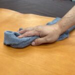 Main nettoyant un tablier en cuir Maison Tanör Paris avec un chiffon doux